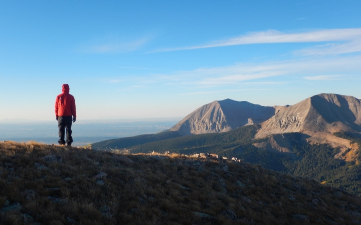 A person faces away from the camera overlooking a vast mountainous landscape.